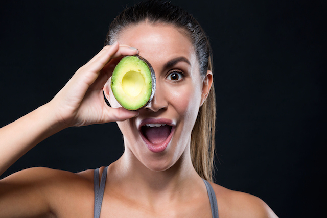 woman with glowing skin holding avocado to face.
