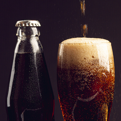 a coke bottle next to a glass filled with soda. 