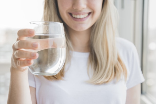 woman smiling holding a glass of water to detox.