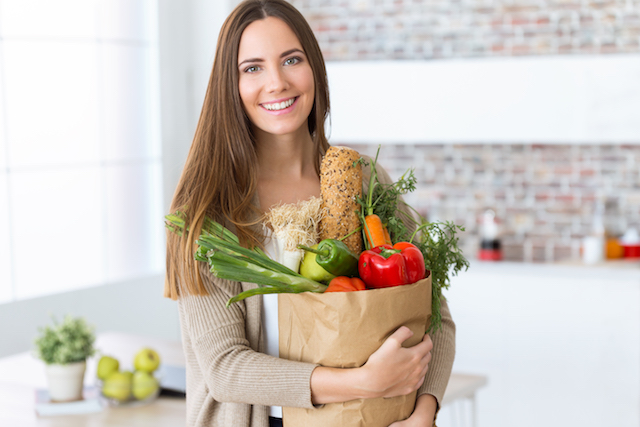 woman smiling holding a bag of produce groceries.